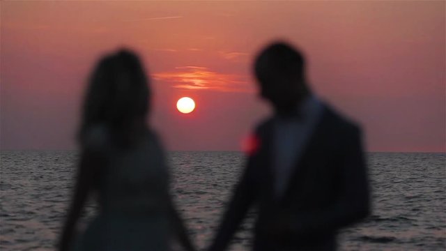 Couple holding hands at sunset sea background love silhouetted close up. Unrecognizable blur honeymoon man and woman stand posing in setting round sun pink sky ocean waves backlit romantic surrounding