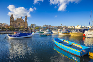 Msida, Malta - Traditional blue painted maltese fishing boat with Msida Parish Church at background on a blue sky summer day