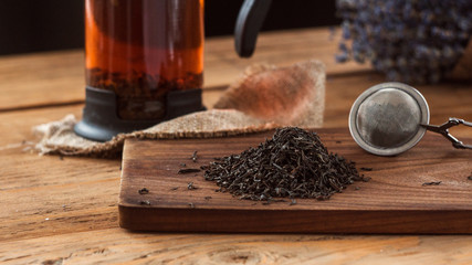 A composition of a tea ball and dry black tea leaves with lavender on wooden board