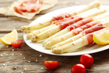 Fresh white asparagus wrapped in jamon on a grey wooden table