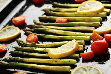 Fresh baked asparagus with lemons and tomatoes on black pan