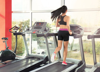 Fototapeta premium Young sporty woman running on treadmill in gym