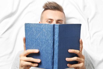 Young man reading book while lying on bed
