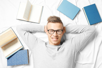 Handsome young man lying on bed among books