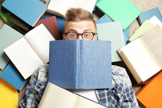 Funny young man lying on floor among books