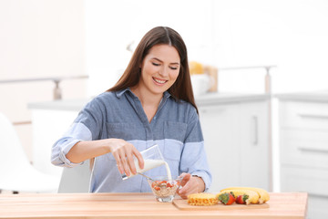 Young woman pouring milk into bowl with breakfast