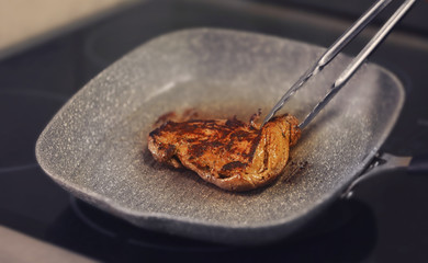 Frying pan with piece of juicy meat on stove, close up view
