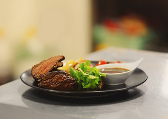 Plate with tasty meat, fried vegetables and sauce on table in restaurant