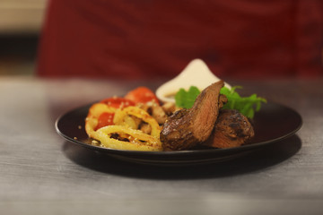 Plate with tasty meat, fried vegetables and sauce on table in restaurant, close up