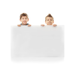 Cute little brothers standing behind board on white background