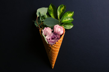 Waffle cone with composition of roses and branches on dark background