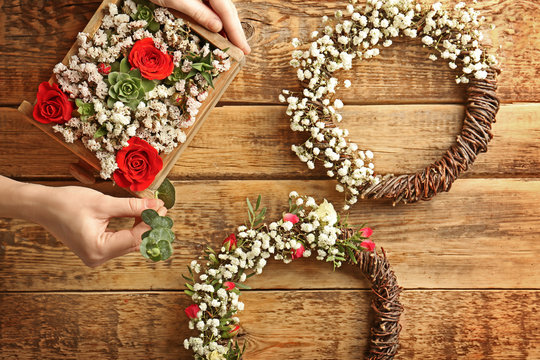 Woman's hands making a flower composition in a square box and two floral wreaths on wooden background