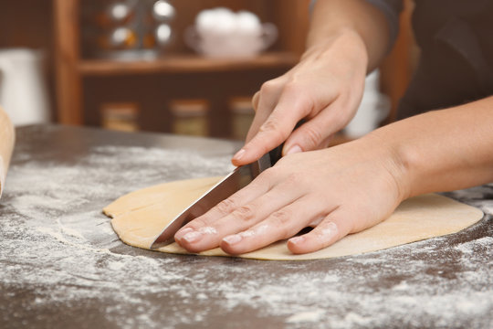 Young woman cutting raw dough in kitchen