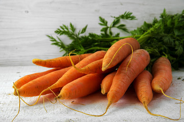 Bunch of organic carrots with green leaves on white painted rustic wood