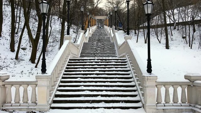 Staircase from the Volodymyrsky Descent to the Monument to the Magdeburg Rights. Stairs and landscape covered with winter snow. IT's snowing and birds are squawking.