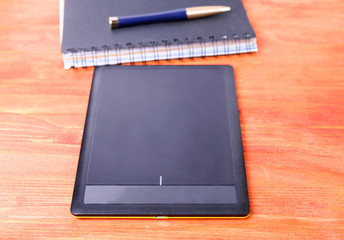 Black tablet, pen, and the diary lying on a wooden table.