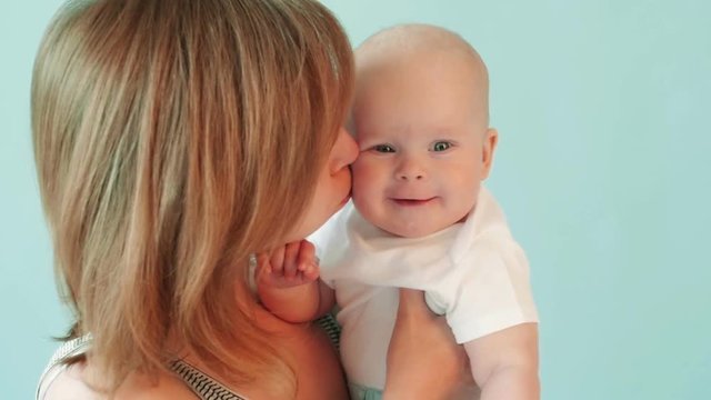 Beautiful woman kisses her son on the cheek on a blue background.