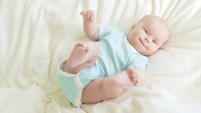 Baby plays with its legs in bed.