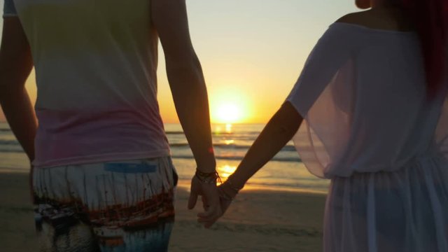 Romantic couple holding hands and walking on the beach towards the sea