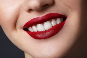 Close-up happy female smile with healthy white teeth, dark red matt lips make-up. Cosmetology, dentistry and beauty care.