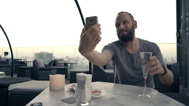 Happy man with cocktail taking selfie photo with cellphone on terrace in bar 
