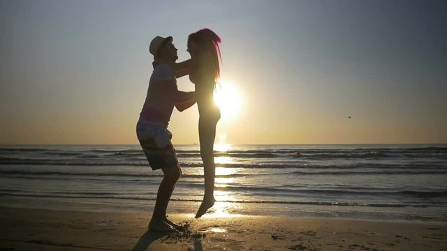 Couple meeting and kissing on shore and woman jumps in her lover arms in slow motion