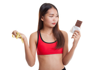 Unhappy Asian healthy girl with chocolate and measuring tape.