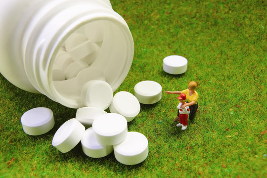 A mother is teaching her son to take medicine on green grass background.