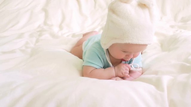 Baby plays with hat strings in bed. 