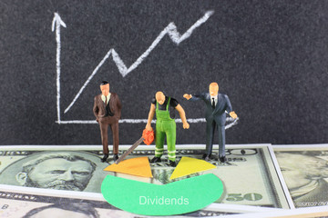 A sawyer is cutting the dividends for two business men. Conceptual image of the word Dividends with dollar background.