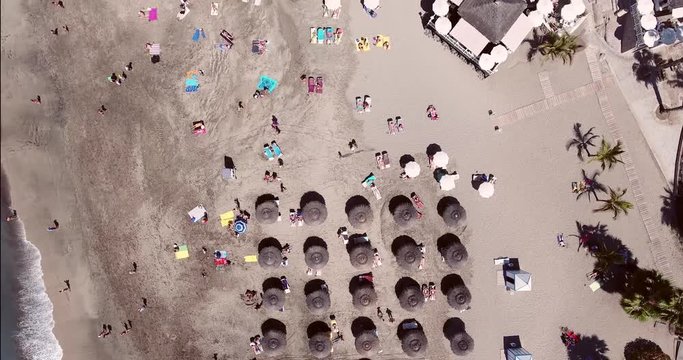 Aerial shot of sea resort beach with umbrellas in rows. Panning shot. Canary Islands beach aerial.