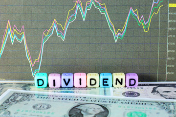 Conceptual image of the word dividend on letter cube with stock graph and dollar background.