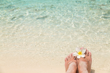 Bare female feet with frangipani flower in the water of the sea