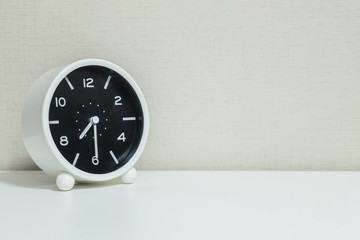 Closeup black and white alarm clock for decorate show show half past seven or 7:30 a.m. on white wood desk and cream wallpaper textured background with copy space