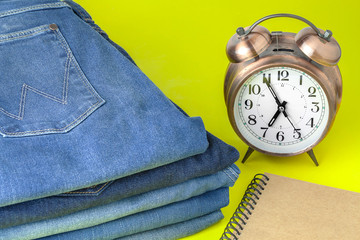 Golden alarm clock and jeans on yellow background