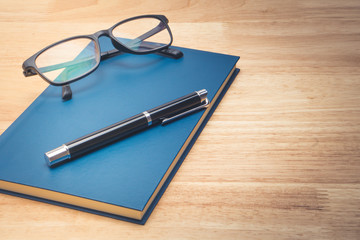 Blue leather notebook and pen on wood background.