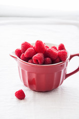Fresh raspberries in a big red ceramic bowl on a white table.