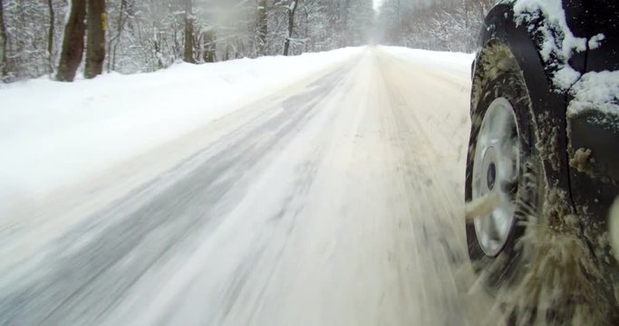Color footage of a car driving on a snowy road, with close up on the wheel.