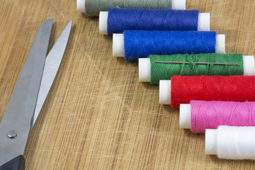 Line of colourful threads with scissors on the light wooden background