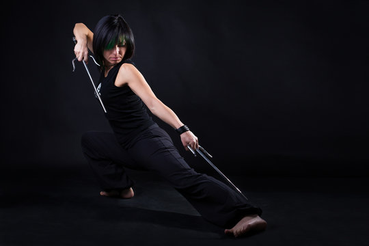 young woman in fighting stance holding a pair of sai: studio portrait on black background