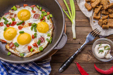 Fred eggs in pan with tomatoes and green fresh onion.
