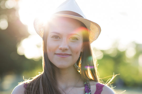 Beauty Romantic Girl Outdoors. Beautiful young brown hair model dressing a white panama hat at park in Sun Light. Summer portrait. Glow Sun, Sunshine. Backlit. Toned in warm colors