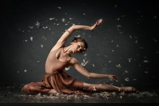 girl dancing barefoot with feathers. ballet. grey background

