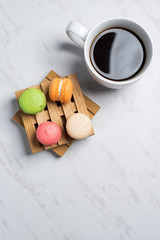 Sweet and colourful macaroons served on little wooden pallets with cup of coffee on a marble texture background. Traditional french dessert. Top view, copy space