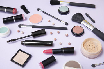 A selection of make up and cosmetic beauty products strewn over a pastel purple background