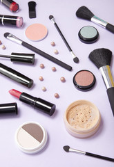 An assortment of make up and cosmetic beauty products strewn over a pastel purple background