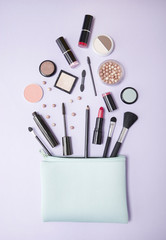 Aerial view of a blue make up bag, with cosmetic beauty products spilling out on to a pastel purple background