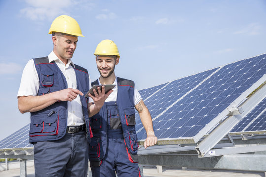 Construction workers next to solar panels looking at digital tablet
