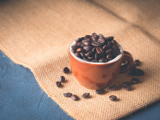 Coffee beans in italian espresso cup on burlap and dark blue black background