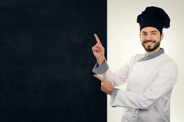 young smiling cook pointing on blank blackboard. copy space